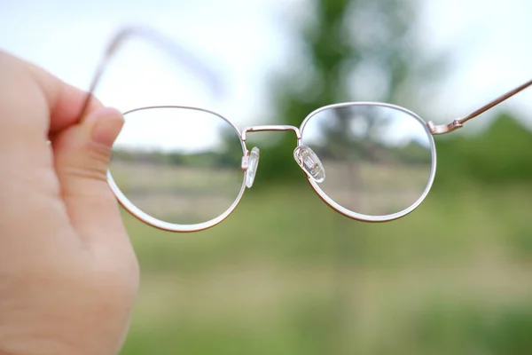 stock image closeup gold-rimmed glasses in female hands, young charismatic man, checks cleanliness and transparency of lenses, concept of eyewear maintenance, optical care, lens hygiene, eyeglass longevity