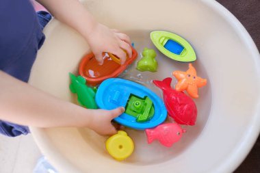 4 yaşındaki mutlu çocuk yüzmek için lastik sarı ördekle, oyuncaklarla renkli balıklarla, havzada kayıkla, etkinlik geliştirme konseptiyle, suyla, yaz eğlencesiyle, sağlıklı yaşam tarzıyla oynuyor.