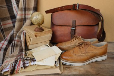 old nostalgic sentimental things, family vintage photographs, stack of books, shoes, leather military satchel on table, checkered grandmother's plaid, family tree, home archive, memory of ancestors