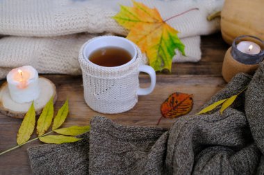 İskandinav usulü sonbahar yassı kucaklaşması, yumuşak yün elbiseli çay, ahşap masa üzerinde sarı yapraklar, mum yanıyor, çay partisi konsepti, güzel hava, sıcak sonbahar havası.