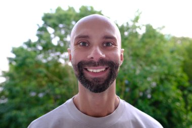 Genç, mutlu, karizmatik bir adam 30-35 yaşlarında, yeşil doğal arka planda gülümseyen, gençliğin güzelliği, pozitif enerjiyi, coşkuyu, manyetik kişiliği vurgulayan, diğerlerini büyüleyen, ilham verici,