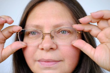 50 yaşında, gözlüklü, uzun saçlı, yaşlılıkla ilgili miyop, kendini kabullenme, hayat dolu ve hayat dolu bir hayat süren yaşlı bir kadının yakın plan kadın yüzü.