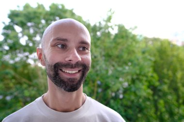 Genç, mutlu, karizmatik bir adam 30-35 yaşlarında, yeşil doğal arka planda gülümseyen, gençliğin güzelliği, pozitif enerjiyi, coşkuyu, manyetik kişiliği vurgulayan, diğerlerini büyüleyen, ilham verici,