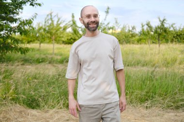 30-35 yaşlarındaki genç adam, modaya uygun gözlükleriyle doğal manzaranın arka planına, doğayla bütünlüğe, doğadan esinlenerek gülümsüyor.