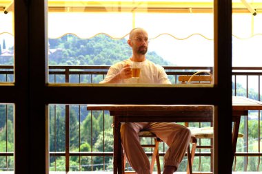 30-35 yaşlarındaki genç adam cam bardaktan çay içer ve pirinç kurabiyesi yer, balkonda çay içer, loggia ılık ışıkla dolar.