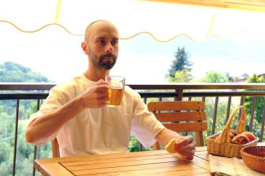 Balkonda çay içmek, loggiayı ılık ışıkla doldurmak, 30-35 yaşlarındaki genç adam cam bardaktan çay içer ve pirinç kurabiyesi yer.