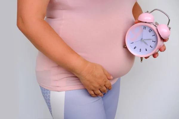 middle-aged pregnant woman holds alarm clock near her belly close-up, waiting for newborn, concept of prenatal contractions, pregnancy reproduction, Pregnancy rate, happy motherhood, selective focus
