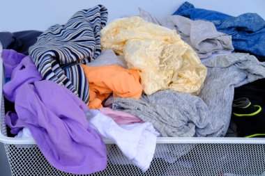 Renkli giysiler rastgele etrafa saçılmış sepet, dağınıklık, soyunma odasında kaos, kıyafet seçimlerinde minimalizm konsepti, sade ve kasıtlı gardırobu desteklemek.