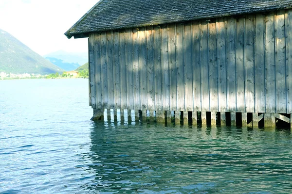 wooden hangar on water, boathouse for boats and boats on stilts, surface of mountain lake Achensee in Austria, Alps mountains in background, concept of recreation and tourism, extreme sports