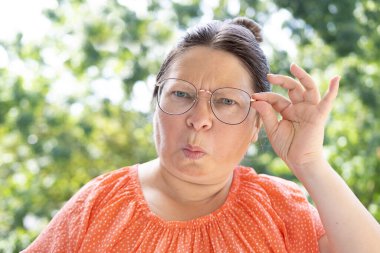 50-55 yaşlarındaki kadın mesafeye bakıyor, kötü görüyor, suratında hoşnutsuzluk görüyor, görsel sağlığını korumak için düzenli göz muayeneleri, kınama züppesi