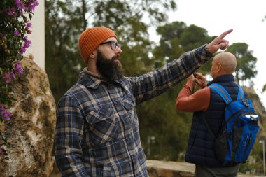 Şapkalı genç adam bir yandan diğer yana bakıyor, ikinci yetişkin beyaz adam fotoğraf çekiyor, turizm konsepti, gezi maceraları, çevre ile turist etkileşimi