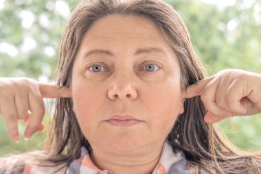 Kafkasyalı 40-45 yaşlarında güzel bir kadın parmaklarıyla kulakları tıkalı, işitsel halüsinasyonlar, kulak ağrısı, işitme kaybı, sağırlık, akut otit medyası, akustik travma, işitsel işleme bozukluğu