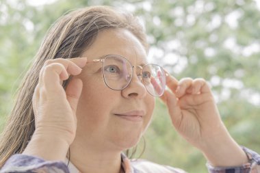 50-55 yaşlarında bir kadın mesafeye bakar, zayıf görür, şaşı olur, gözlük takar, olgun kadın yüzünü, miyopluğu, görüş düzeltmesini kapatır.