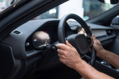 Kokpit, sürücü koltuğunda erkek eli direksiyonda elektrikli araba, modern yolcu vagonu, gösterişli iç mekan kontrol tekerleği, vites kolu, ön cam ve ön panel.