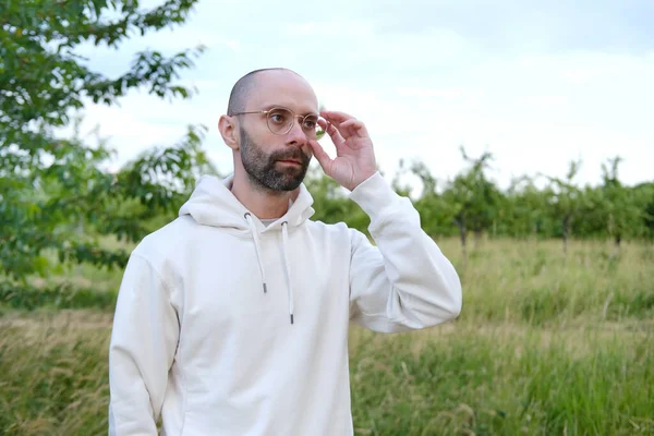 30 yaşında, gözlüklü sakallı genç adam merceklerden bakıyor, insan sağlığı kavramı, yetişkinlikte iyimserlik, görsel sağlığını korumak için düzenli göz muayenesi.