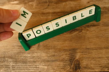Yakın plan kadın eli kare tahta alfabe blokları tutuyor. İmkansız kelimesi, klasik arka plan, kendini tanıtma, kendini motive etme ve mutluluk, yaratıcı anlam üzerinde kelimelere dönüşüyor.