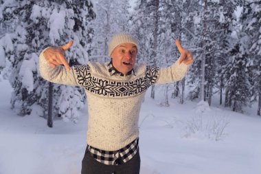 Olgun karizmatik bir adam 60 yıl şapkalı ve İskandinav süveteri giyen neşeli bir şekilde etrafta geziyor, kış ormanlarında kar yığınlarının arka planına karşı yüzünü buruşturuyor, aktif yaşam tarzı kavramı, iyi ruh hali.