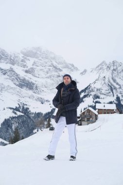 Kışlık giysiler içinde genç düşünceli bir adam, 30 yaşında İsviçre 'deki kar örtülü dağlara karşı, popüler turizm merkezleri kavramı, güzel karlı dağ zirveleri ve doğal harikalar.