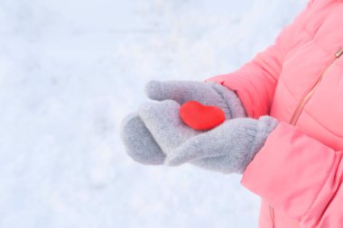 Pembe ceketli bir kız elinde aşkın sembolü ellerinde gri yün eldivenler, kış arkaplanı ve beyaz kar, günah çıkarma konsepti, sevgililer günü konsepti.