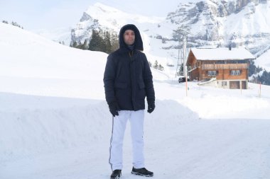Kışlık giysiler içinde genç düşünceli bir adam, 30 yaşında İsviçre 'deki kar örtülü dağlara karşı, popüler turizm merkezleri kavramı, güzel karlı dağ zirveleri ve doğal harikalar.
