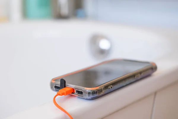 phone charging on edge of bathtub, concept Dangers of Electronics in Wet Areas, Preventing Water-Related Accidents, Electrical Hazards at Home