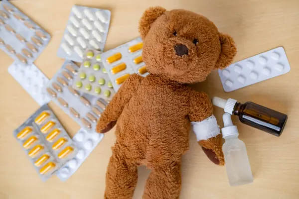 teddy bear with bandaged arm, surrounded by scattered medicines and pills, health, care and treatment children through soft toy, medical therapy and pediatrics