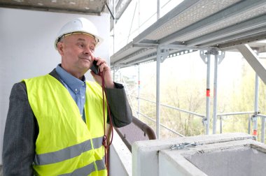 Tecrübeli bir inşaatçı, inşaat ekibi şefi, miğfer koruma mühendisi inşaat inşaatı için inşaat alanında telefonla konuşuyor, inşaat mühendisliği konsepti.