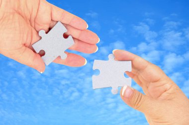 İki el arka plandaki iki yapboz parçasını birleştirmeye çalışıyor. Takım çalışması konsepti. Yapbozu birbirine bağlayan yapbozun yakın eli
