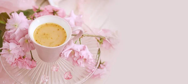 cup with drink coffee cappuccino, hot chocolate with milk, sakura flowers, caffeine improves functioning of human brain, stimulates nervous system, health benefits and harms, copy space, banner