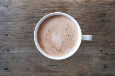 Kahverengi ahşap bir masa üzerinde kahve kapuçinosu olan beyaz fincanın yakın çekimi, sabah kahvesi, kafein bağımlılığı, enerji takviyesi, üst görünüm, tasarımcılar için kopyalama alanı