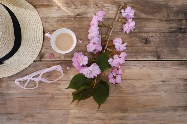 cup with drink coffee cappuccino, hot chocolate with milk, light sunhat, pink sakura flowers, caffeine improves functioning of human brain, stimulates nervous system, health benefits and harms