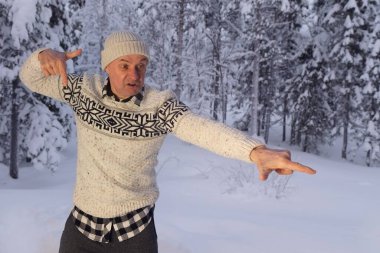 Olgun karizmatik bir adam 60 yıl şapkalı ve İskandinav süveteri giyen neşeli bir şekilde etrafta geziyor, kış ormanlarında kar yığınlarının arka planına karşı yüzünü buruşturuyor, aktif yaşam tarzı kavramı, iyi ruh hali.