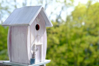 Beyaz boyalı kuş evi yeni bahar sezonu için hazır. Baharın arka planında, ağaçların yeşil yapraklarına karşı bir ev. Kuş yuvası konsepti.