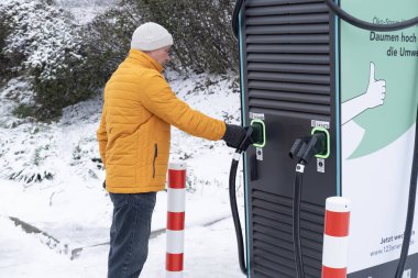 DC konnektörü elinde tutan adam, elektrikli araç birleşik şarj sistemi CCS2 hızlı şarj istasyonu, kışın alternatif enerji, teknoloji ve yenilik, Frankfurt - 21 Ocak 2024