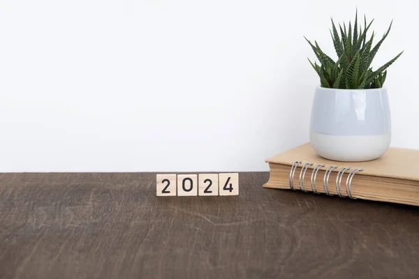 Wooden letters spelling date 2024, notebook, daily planner on vintage wooden table, potted indoor plant, Time Management, Planning, office aesthetics and business settings