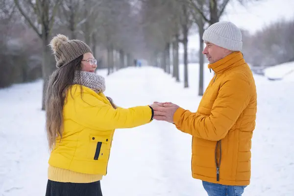 Happy couple in yellow jackets in winter park, hands frozen, man warming womens hands, rub cold palms on walk, overall family health strategies, Winter Romance, Love in Snow, Seasonal Happiness