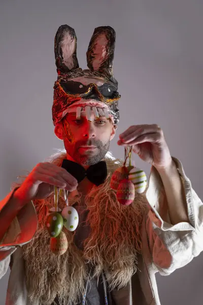 creepy Bunny Easter man, Happy attractive young guy in cringe rabbit monster mask holding Easter eggs, looking at camera, Happy holiday and funny easter day concept, Humor and Creative Celebration