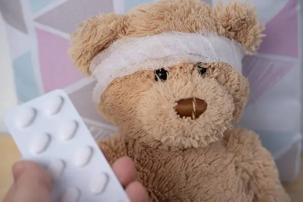 teddy bear with bandaged head, doctor\'s hand holding out blister pack of pills, health, care and treatment children through soft toy, medical therapy and pediatrics