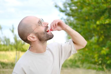Bej tişörtlü komik, genç karizmatik adam lezzetli kırmızı kirazlar yiyecek, konsept vejetaryen yiyecekler sağlıklı beslenme, vitaminle zenginleştirilmiş yiyecekler.