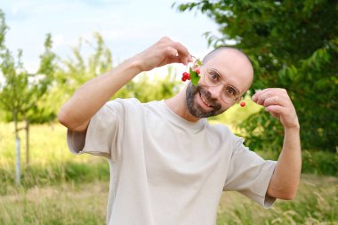 Bej tişörtlü komik, genç karizmatik adam lezzetli kırmızı kirazlar yiyecek, konsept vejetaryen yiyecekler sağlıklı beslenme, vitaminle zenginleştirilmiş yiyecekler.