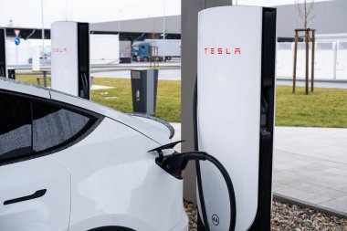 Beyaz Tesla elektrikli otomobili şarj istasyonunda aküyü yeniliyor, alternatif enerji gelişimi, Çevresel sürdürülebilirlik, Berlin, Almanya 'da icat otomotiv endüstrisi - 19 Şubat 2024