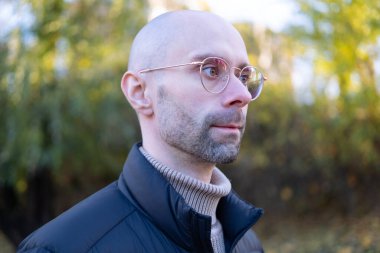 30-35 yaşlarında, ceketli, şık gözlüklü, doğal arka planda, gençlik kültürü ve Stereotipli, genç nesil, giysiler, aksesuarlar, açık hava aktiviteleri...