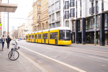 Berlin 'de şehir caddesinde ilerleyen sarı tramvay ön binalar, seyahat, turizm ve şehir molaları, çevre dostu toplu taşıma ve şehir planlaması, Berlin, Almanya - 18 Şubat 2024