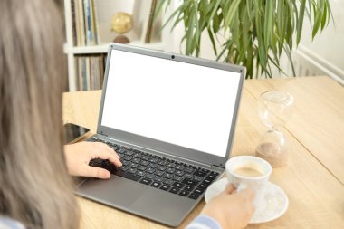 Bayan öğrenci iş kadını boş bir makete bakıyor, elinde fincan kahve, reklam için beyaz dizüstü bilgisayar ekranı, sanal toplantı, uzaktan çalışma, internette arama, webinar izleme