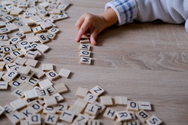 Çocuğun küçük elleri, anneyi hecelemek için ahşap harfleri dikkatlice düzenler, sevgi ve minnettarlığın iç açıcı ifadesi, erken edebiyat gelişimi.