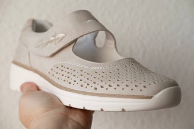 Yeni bej deri ayakkabı, kadın ellerinde rahat delinmiş mokasen, yeni kadın ayakkabıları almak, ağrıyan ayaklar için modern doğal ayakkabılar, eklem problemleri, açık hava yürüyüşleri için