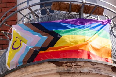 Gökkuşağı gurur bayrağı balkon evinde ilerliyor. Siyah, kahverengi ve mavi çizgiler sembol şeklinde. Daniel Quasar tarafından yaratıldı, Uluslararası LGBT hareketi, Gurur Ayı