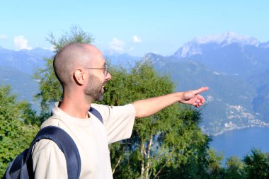 Genç adam, sırt çantalı turist zorlu bir hedef olduğunu gösteriyor. Kayalık yolda yürüyüş, konsept yaz tatili deneyimi, yol macerası.