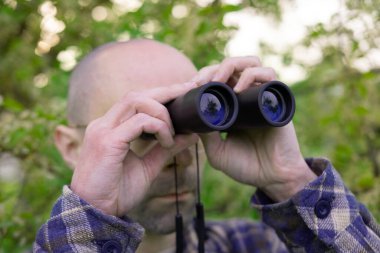 Genç adam, yemyeşil alanlarda gizlenmiş casuslar dürbünle eş zamanlı giyiniyor, özel dedektif gözetleme yapıyor, heyecan arayanların izini sürüyor.