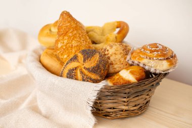 Peynirli çörekler, haşhaşlı çörekler, rulo ekmekler, tuzlu krakerler ve geleneksel hasır sepetinde tatlı kaymaklı tartlar içeren lezzetli ev yapımı hamur işleri.